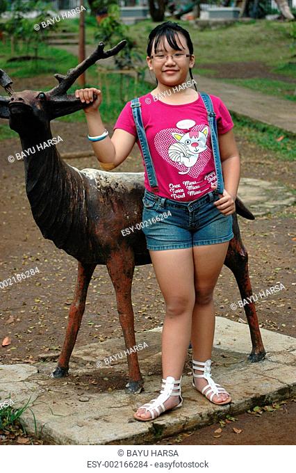 little girl stand up beside deer statue