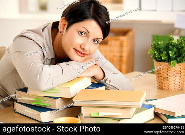 Tired young woman learning at home, resting on pile of books