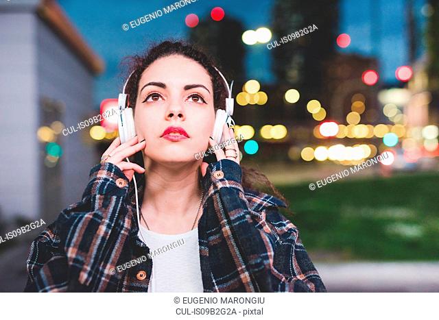 Woman wearing headphones in the city looking up, Milan Italy