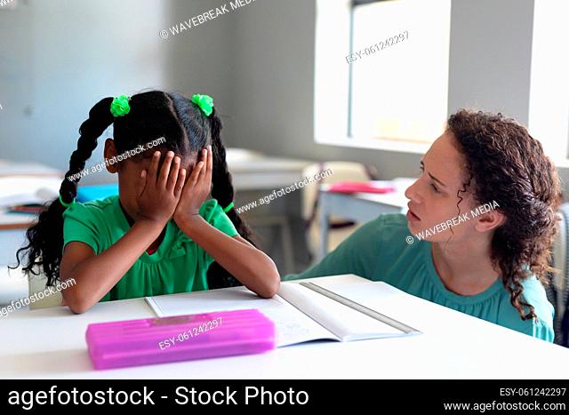 Caucasian young female teacher looking at african american elementary schoolgirl with hand on face