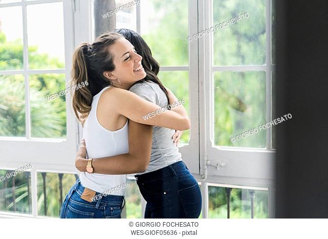 Two happy girlfriends hugging at the window