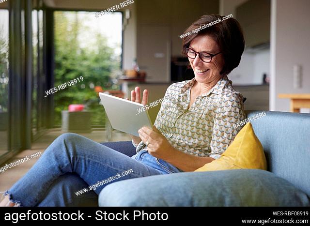 Happy woman waving on video call through tablet PC at home