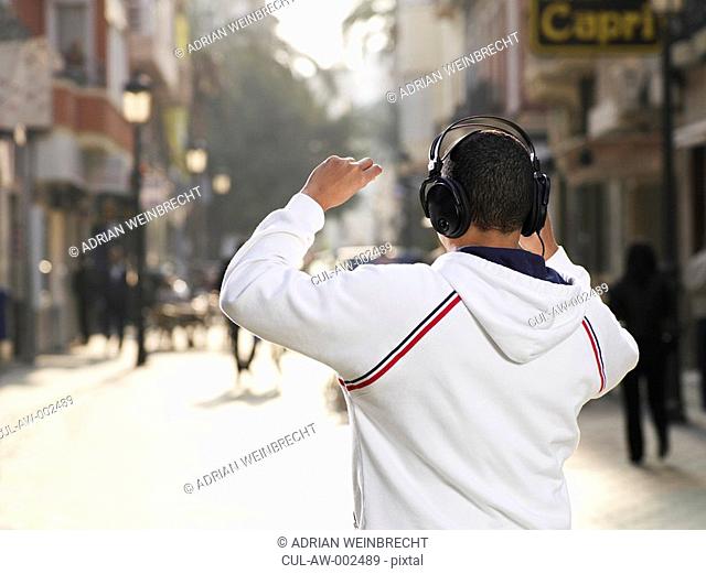 Young man standing in street wearing headphones, rear view