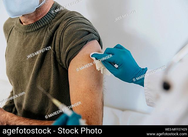 Healthcare worker cleaning arm of male patient while preparing for vaccination at examination room