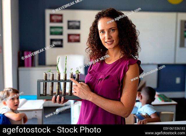 Portrait of caucasian young female teacher showing seedlings test tubes while teaching in classroom