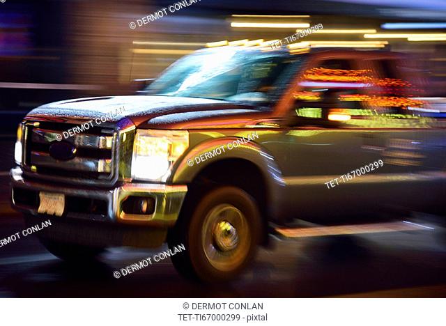 Truck in illuminated city street, in motion at night