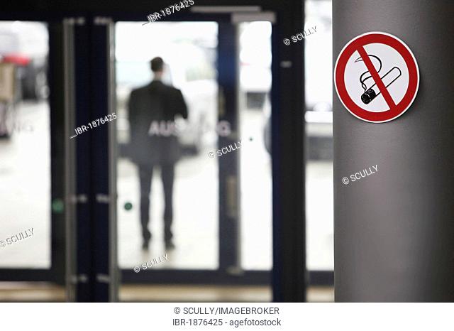No smoking sign and a man smoking in front of an office building