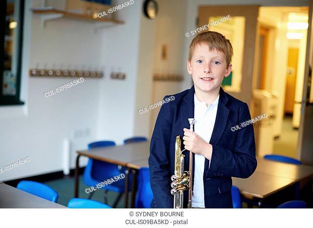 Primary schoolboy holding trumpet in classroom, portrait
