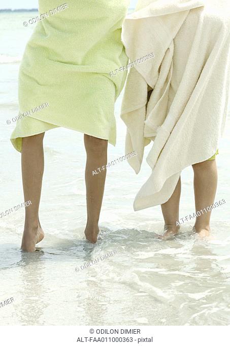 Children wrapped in towels standing in surf, low section