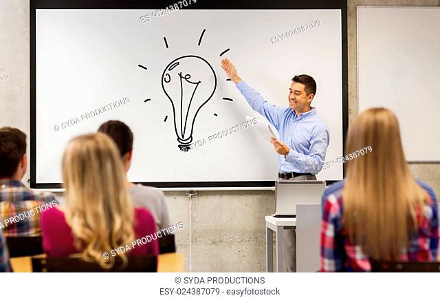 education, high school, teaching, idea and people concept - group of students and happy teacher with notepad showing light bulb drawing on white board in...