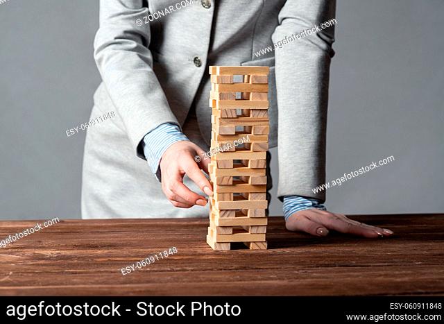 Businesswoman removing wooden block from tower on table. Management of risks concept with wooden jenga game. Business development and assistance