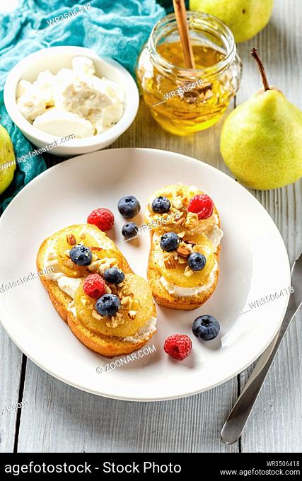 Crostini with ricotta cheese, fried pear, nuts and honey, decorated with raspberries and blueberries