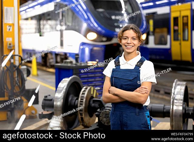 Smiling young trainee standing with arms crossed in warehouse at factory