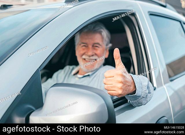 Happy owner looking at the camera with happy face and thumbs up. Handsome bearded mature man sitting relaxed in his newly bought car looking out the window...