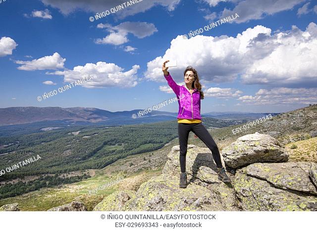 sport hiking or trekking woman with purple jacket, standing on rock peak, with mobile smart phone taking selfie photo picture