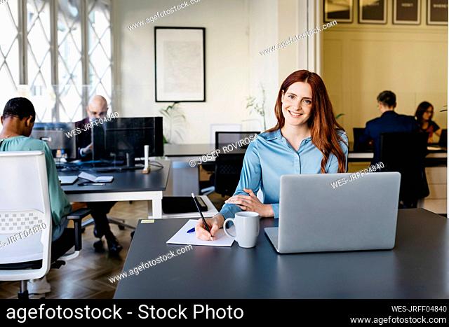 Smiling businesswoman writing in paper at office desk