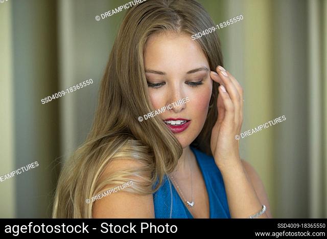 Beautiful young woman with striking blue eyes and vivid red lips, looking down while fixing her hair