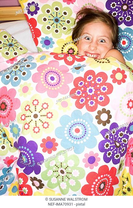 A happy girl lying under a flowery quilt Sweden