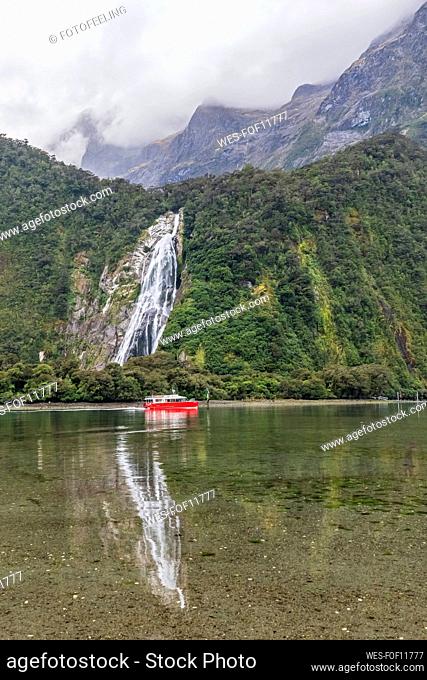 New Zealand, Oceania, South Island, Southland, Fiordland National Park, Waterfall and boat on water