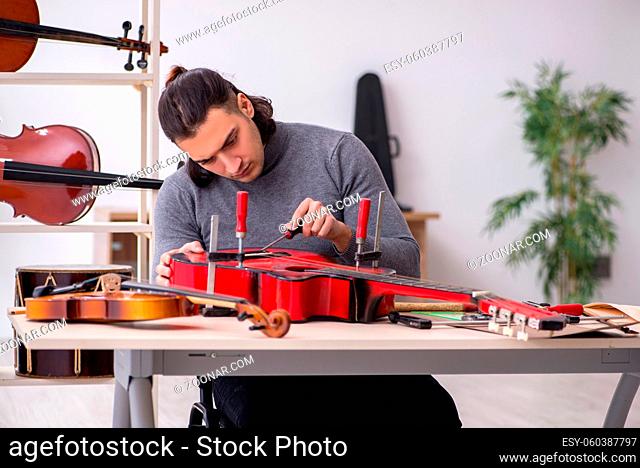 Young male repairman repairing guitar in workshop