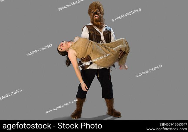 Wolfman werewolf holding a dead woman and lover, in his arms with a distraught and sad expression on his face, two people in Halloween costumes on gray...