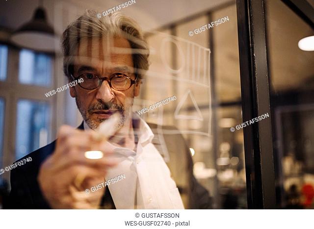 Senior businessman drawing on glass pane in office