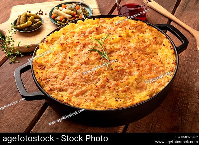 Shepherd's pie in a cooking pan with pickles, herbs, and red wine, on a dark rustic wooden background