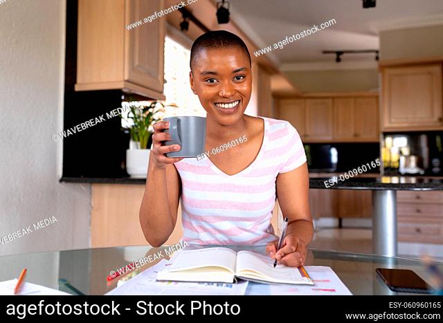 Portrait of happy biracial businesswoman with cup telecommuting at home office