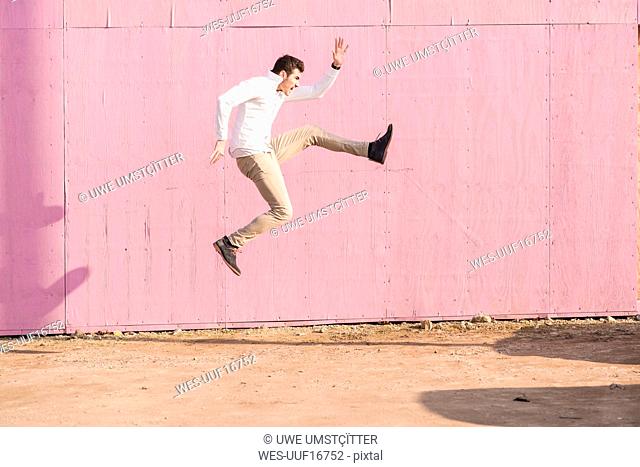 Exuberant young man jumping in front of pink wall