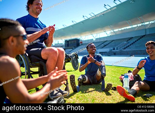 Paraplegic and amputee male athletes clapping on sunny stadium grass