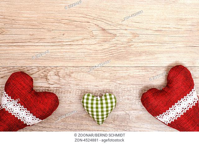 Textfreiraum für Glückwünsche auf einem Holzbrett mit drei Herzen aus Stoff