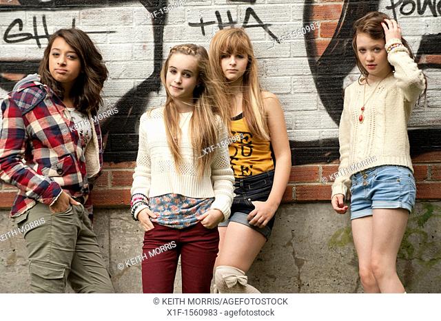 A group of 13 year old teenage girls moody with attitude standing in front of a graffiti covered wall UK