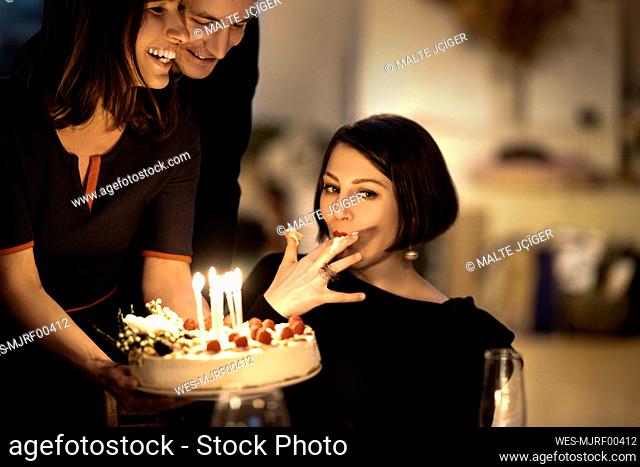 Beautiful woman eating cake by male and female friends during celebration at home