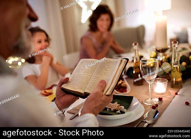 Happy small girl with grandparents sitting indoors celebrating Christmas together, bible reading
