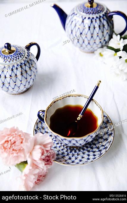 A cup of black tea, cloves and a decorative teapot on a set table