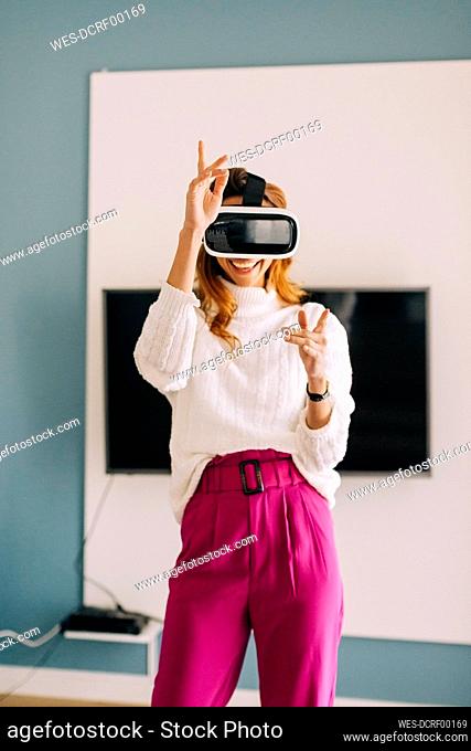 Happy young woman wearing VR glasses at home
