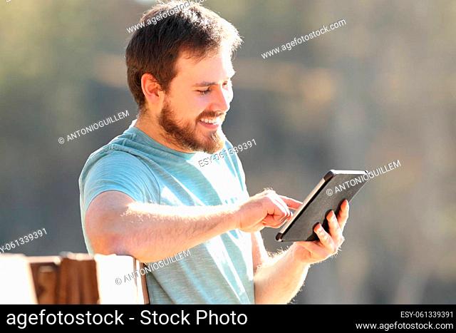 Happy man checking online tablet content outdoors a sunny day