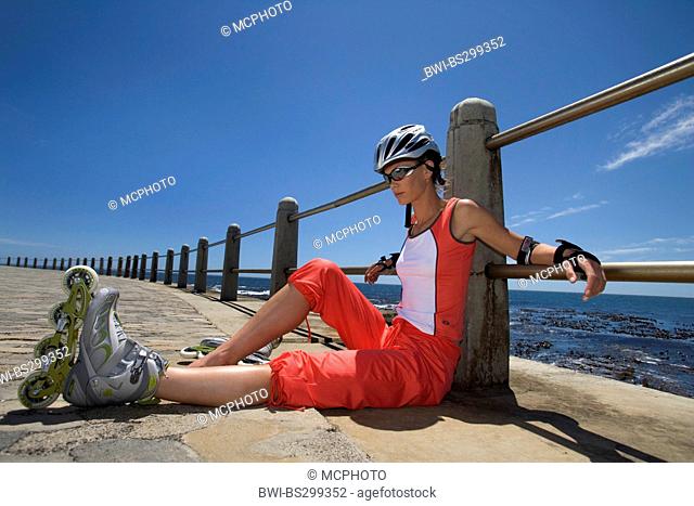 inline skater leaning at a railing sitting on the paved ground of a promenade