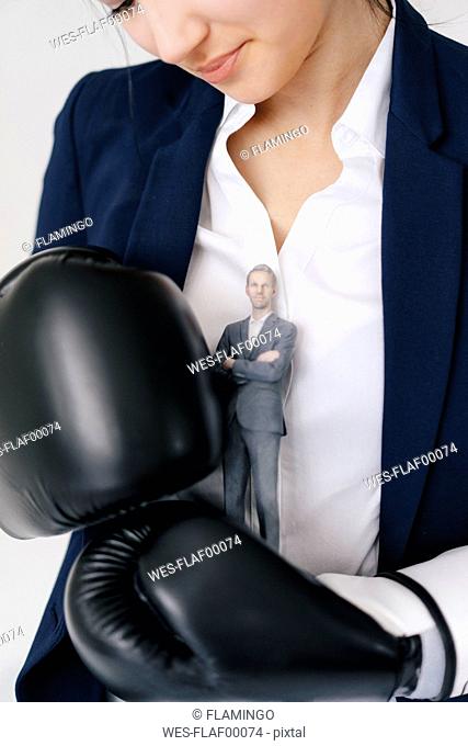 Businesswoman holding businessman figurine between boxing gloves