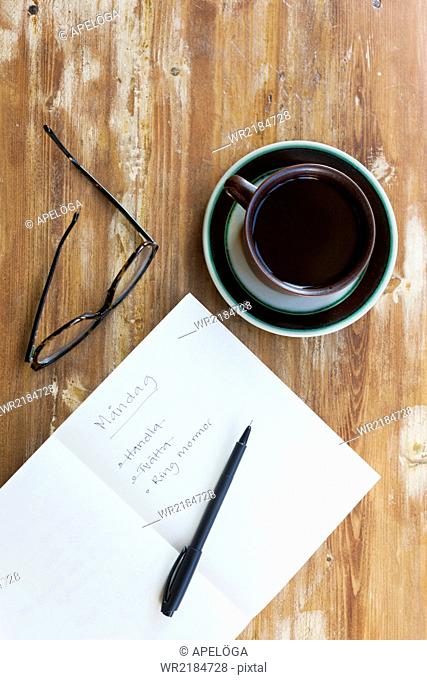 Directly above shot of Monday checklist with glasses and black coffee on wooden table