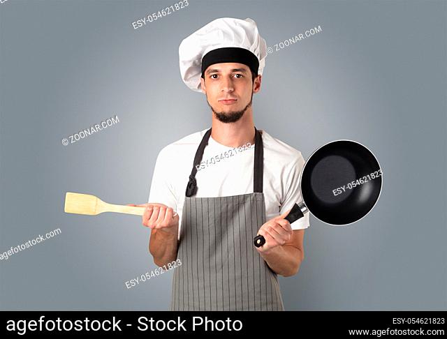Young bearded cook portrait with kitchen tools and empty wallpaper