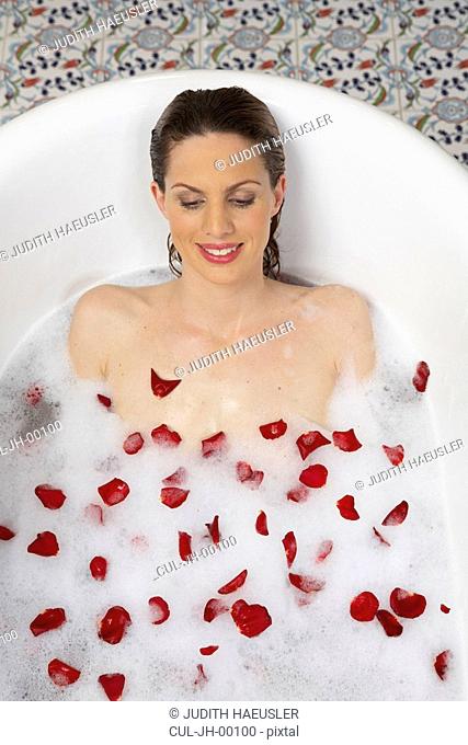 young woman lying in bath with lather and rose petals, overhead view