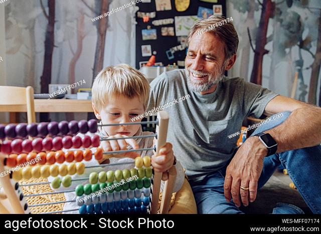 Happy father watching son counting abacus in bedroom