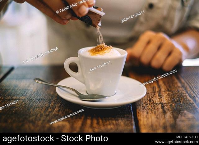 close up hands putting white sugar in an italian espresso coffee at the bar or restaurant ona wooden table. italian tradition and arabic