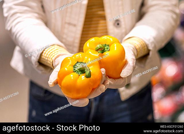 Crop view of young woman with protectice gloves holding yellow bell peppers