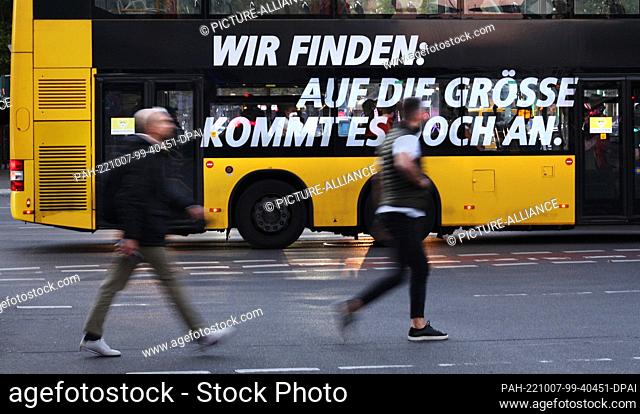 06 October 2022, Berlin: 06.10.2022, Berlin. Two young men walk in front of a double-decker bus of the BVG in Steglitz in front of the town hall Steglitz over a...