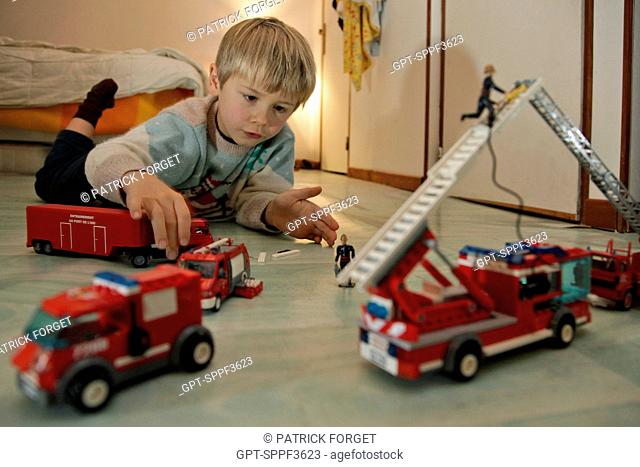 LITTLE BOY PLAYING IN HIS BEDROOM WITH TOY FIRE ENGINES, A PROFESSION THAT FASCINATES CHILDREN, FRANCE