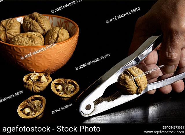 Handful of walnuts in orange ceramic bowl, walnuts broken and hand with nutcracker on black background