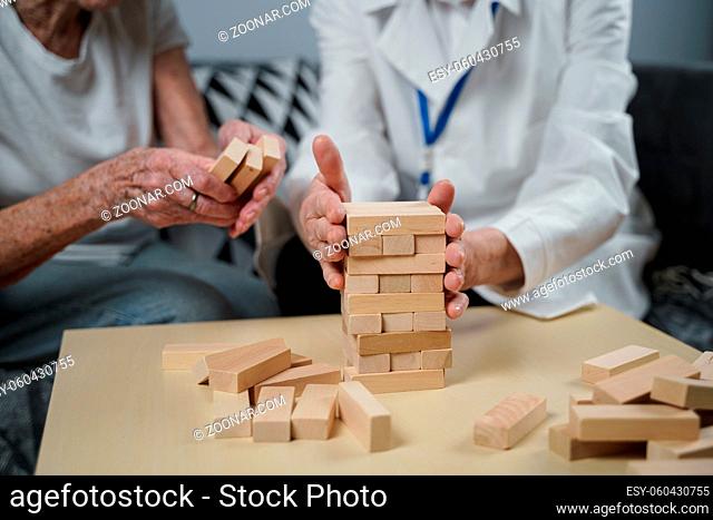 Senior woman practice skills, build wooden blocks, build tower and try not to let it fall, Jenga game. Old patient pull out block, place on top