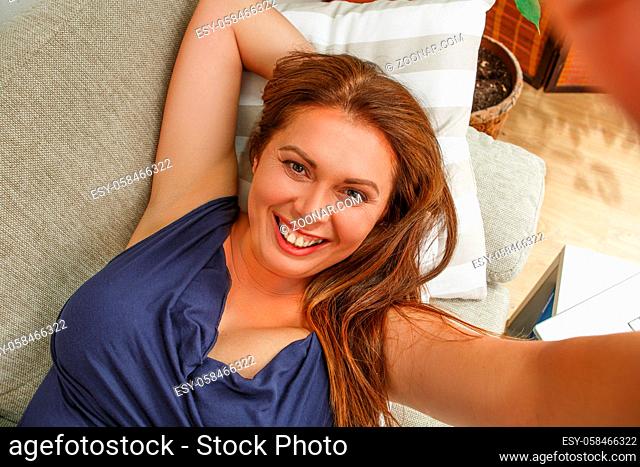 Portrait of beautiful woman with red lips making selfies at home. Totthy smiling lady lying on sofa or couch